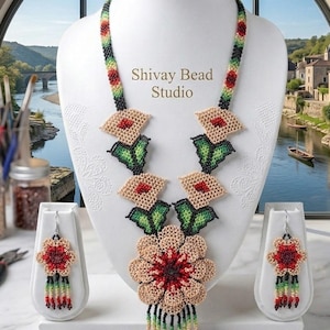 May include: A beaded jewellery set featuring a necklace and matching earrings. The necklace has a large central flower pendant with red, beige, and black beads, accented by smaller floral motifs and a beaded fringe. The text Shivay Bead Studio is visible.