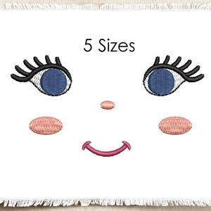 Könnte beinhalten: Ein Stickmuster, das ein Gesicht mit zwei blauen Augen, langen schwarzen Wimpern, einer kleinen rosa Nase, zwei ovalen rosa Wangen und einem geschwungenen rosa Mund zeigt. Der Text 5 Sizes steht zentriert über den Augen auf weißem Stoff mit Fransen.