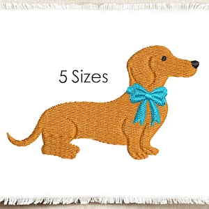 May include: An embroidery design of a brown dachshund dog in profile, featuring a bright cyan blue bow tied around its neck. The text "5 Sizes" is printed in black above the dog's back. The entire design is set on a white fabric background.