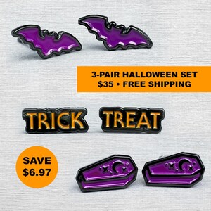 May include: A set of three pairs of enamel pins featuring purple bats, black pins with orange text reading TRICK TREAT, and purple coffin-shaped pins with black crescent moon and star details. The pins have black metal outlines.