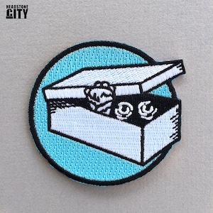 May include: A white embroidered box with a black lid and a blue background. The box is open and has a few items inside. The box is surrounded by a black outline.