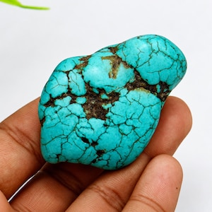 Puede incluir: Una piedra de turquesa pulida de color azul cian vibrante con una red compleja de vetas de matriz de color marrón oscuro en forma de telaraña que recorren su superficie lisa y redondeada, mostrando patrones minerales naturales.