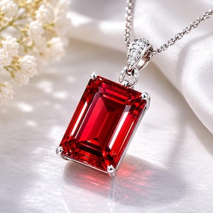 Può includere: Un ciondolo rettangolare con pietra preziosa rossa sfaccettata, incastonato in una montatura in metallo color argento con quattro griffe. Il ciondolo presenta una contromaglia decorativa ornata da piccole pietre rotonde trasparenti e una sottile catenina color argento.