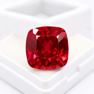 Peut inclure: Une pierre précieuse rouge vif et profonde avec une taille coussin et une surface à facettes qui reflète la lumière. La pierre présente une forme carrée aux coins arrondis, mettant en valeur une teinte cramoisie saturée et brillante.