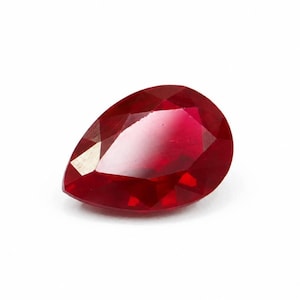 Peut inclure: Une pierre précieuse en forme de poire d'un rouge profond et vibrant avec une surface à facettes. La pierre présente un sommet pointu et une base arrondie, reflétant la lumière sur ses multiples surfaces polies pour un aspect brillant.