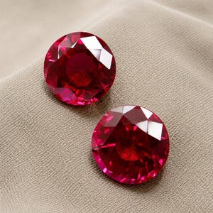 Peut inclure: Deux pierres précieuses rondes, facettées et d'un rouge profond avec une taille brillant. Les pierres présentent une teinte cramoisie vibrante et des facettes géométriques claires qui reflètent la lumière sur leurs surfaces circulaires.