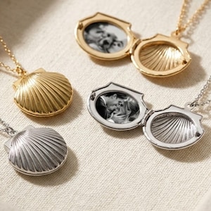 Könnte beinhalten: Vier muschelförmige Medaillons an zarten Ketten, darunter zwei geschlossene Anhänger in Gold- und Silbertönen sowie zwei geöffnete Medaillons, die schwarz-weiße Fotografien zeigen. Die Metalloberflächen weisen eine gerippte Struktur auf.