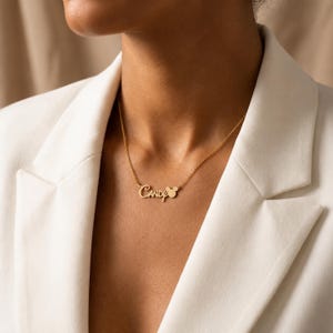 May include: A gold-toned metal necklace featuring a delicate chain and a personalised nameplate pendant that displays the name Candy in a cursive script font, with a small circular icon resembling a mouse head silhouette attached to the end.