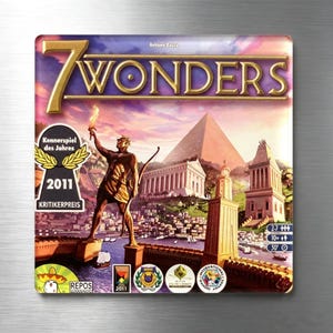 Peut inclure: La boîte du jeu de société 7 Wonders présente une illustration colorée d'une cité antique avec une grande statue tenant une torche, une pyramide et une architecture classique. Le titre 7 Wonders est imprimé en lettres dorées en haut.