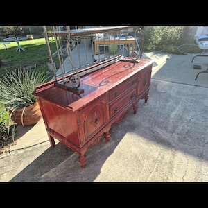 Puede incluir: Un aparador de madera roja antigua con tres cajones y tallas ornamentadas. Tiene un acabado brillante y se apoya en cuatro patas decorativas. Una rejilla de metal está unida en la parte superior.