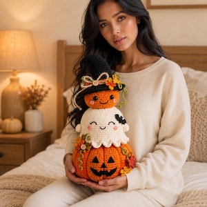 May include: A stacked crochet plush toy featuring a large orange jack-o'-lantern base, a white ghost in the middle, and a small orange pumpkin wearing a black witch hat on top. The design includes decorative wooden buttons, vines, and leaves.