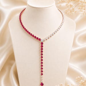 Puede incluir: Un collar en forma de Y con una cadena metálica engastada con piedras de corte redondo. Un lado del collar y la caída vertical están adornados con piedras de color rojo intenso, mientras que el otro lado presenta piedras claras e incoloras.