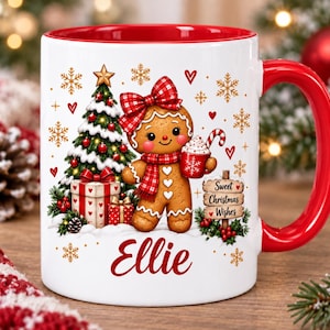 May include: A white ceramic mug with a red interior and handle, featuring a gingerbread person wearing a red plaid bow and scarf, a Christmas tree, gifts, and a sign that reads Sweet Christmas Wishes, with the name Ellie printed in red.