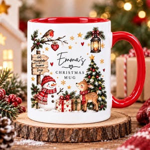 May include: A white ceramic mug with a red interior and handle, featuring a festive illustration of a snowman, a reindeer, a Christmas tree, a lantern, and a robin. The text reads Emma's CHRISTMAS MUG and Hot Chocolate Happier Days.