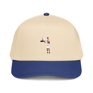 May include: A beige baseball cap with a blue brim and a small graphic on the front center depicting a basketball player in a white uniform jumping to shoot a basketball into a hoop. The cap features a blue button on the top crown.