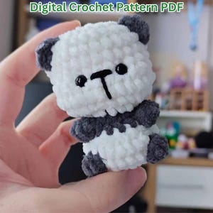 May include: A small, plush, white and dark gray crocheted panda toy with black plastic bead eyes and a stitched black nose and mouth. The text Digital Crochet Pattern PDF is visible at the top of the image, indicating a downloadable file.