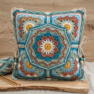 May include: A square, crocheted pillow in shades of teal, blue, brown, yellow, and cream. The pillow features a central floral design and smaller floral motifs in each corner. Decorative ties with wooden beads secure the pillow.