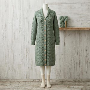 May include: A sage green long-sleeve knit cardigan featuring a shawl collar, a button-down front with nine light brown buttons, and an intricate vertical cable knit pattern throughout the garment, displayed on a mannequin.