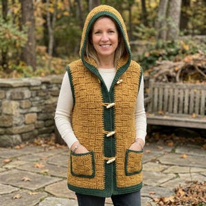 May include: A mustard yellow hooded waistcoat featuring a textured basketweave crochet pattern, dark green trim, and three light-coloured wooden toggle buttons down the front. The sleeveless garment includes two square front pockets and a hood.