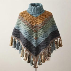 May include: A crochet turtleneck poncho featuring a chevron pattern with horizontal stripes in shades of mustard yellow, sage green, light blue, and charcoal gray. The hem is finished with multiple hanging tassels adorned with small white beads.