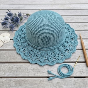 Peut inclure: Un chapeau au crochet bleu sarcelle avec une calotte arrondie et un large bord festonné orné d'un motif en forme d'étoile. Le chapeau est accompagné d'un crochet en bois, d'une aiguille à coudre en métal et d'un fil assorti.