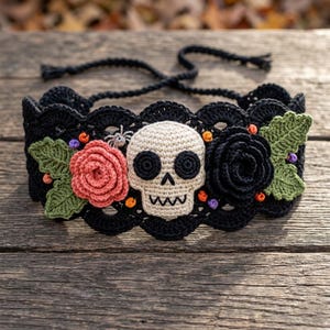 May include: A black crocheted choker featuring a central beige skull, a pink rose, a black rose, green leaves, and a small spider. The piece has a scalloped edge and thin black ties for closure, accented with tiny orange and purple spherical beads.