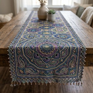 May include: A handcrafted, colorful table runner with a detailed crochet design. The runner features a geometric pattern in shades of blue, purple, green, and gold. The edges are finished with a beaded fringe, adding a decorative touch to this home decor item.