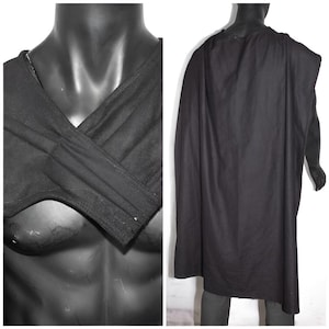 May include: A black cape featuring a wrap-style front with overlapping fabric panels that cross over the chest. The garment hangs from the shoulders, extending down the back in a long, solid black panel of fabric with a smooth, matte texture.