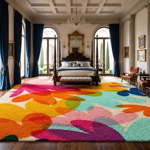 May include: A large, colorful area rug with a floral design dominates a luxurious bedroom. The rug features large, abstract flower shapes in shades of orange, yellow, pink, and blue. The room includes a four-poster bed, chairs, and large windows with blue curtains.