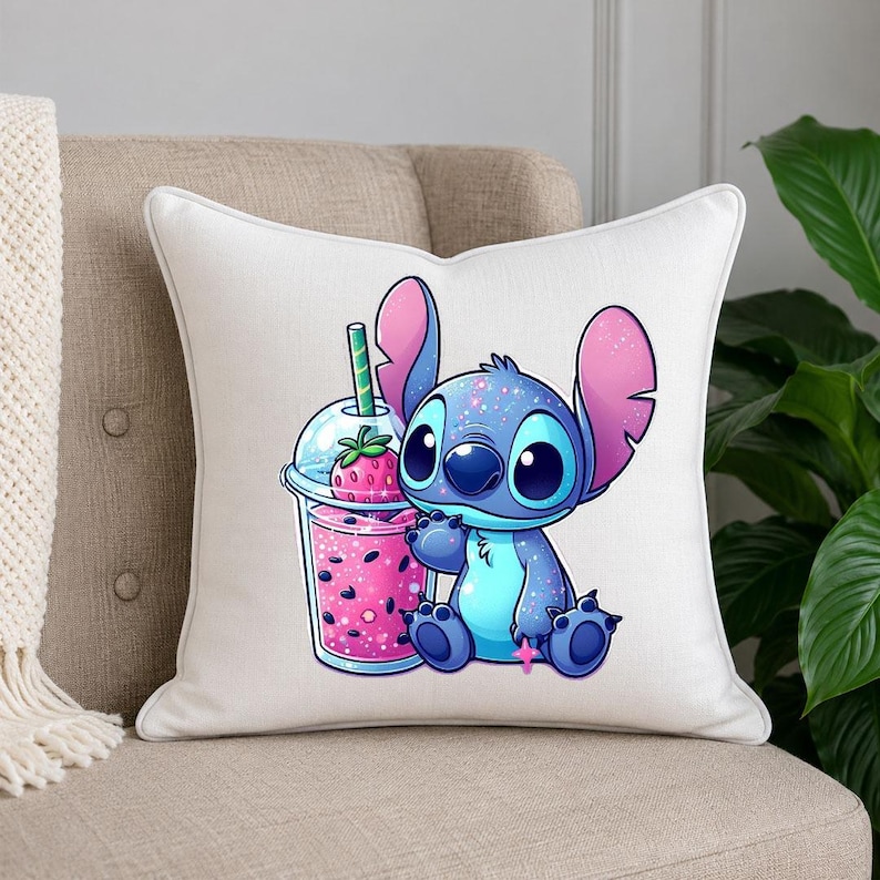 May include: A white square throw pillow featuring a colorful graphic of a blue alien character with large ears sitting next to a clear plastic cup filled with a pink strawberry drink, complete with a green straw and a strawberry garnish.