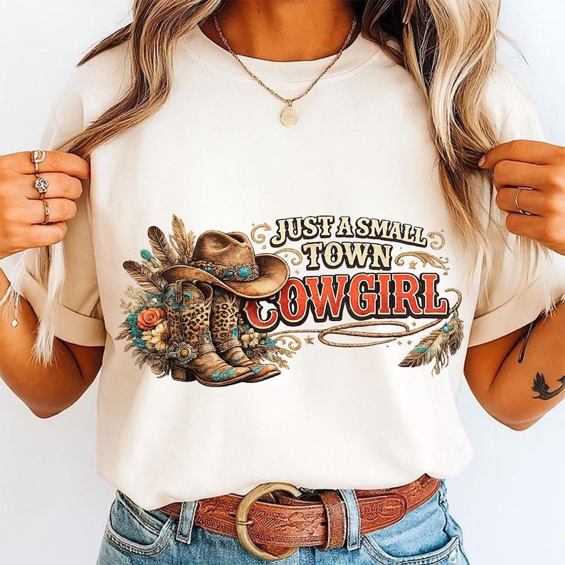 Pu&ograve; includere: Una t-shirt color crema con una stampa grafica di un cappello da cowboy marrone e stivali abbinati con dettagli leopardati, circondati da piume e fiori. Il testo recita JUST A SMALL TOWN COWGIRL in un carattere stilizzato, grassetto, rosso e nero.