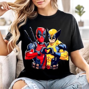 May include: A black short-sleeved t-shirt featuring a graphic print of the characters Deadpool and Wolverine standing side by side. Deadpool is in a red and black suit with swords on his back, while Wolverine wears a yellow and blue suit.