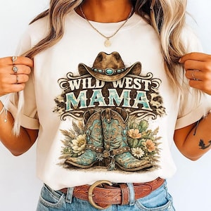 Pu&ograve; includere: Una t-shirt color crema con una stampa grafica raffigurante un cappello da cowboy marrone sopra la scritta "WILD WEST MAMA" in turchese e marrone, con un paio di stivali da cowboy turchesi, fiori del deserto e cactus sotto.