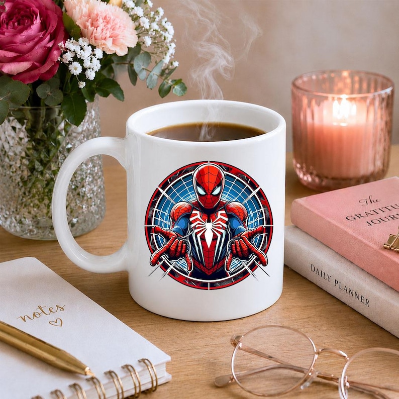 May include: A white ceramic mug featuring a circular graphic of the superhero Spider-Man in a red and blue suit with a white spider emblem on the chest, shown in a dynamic pose with hands extended forward against a blue webbed background.