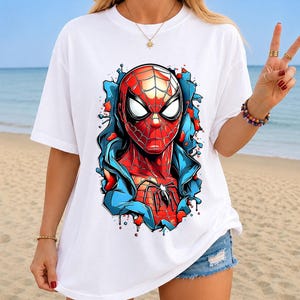 May include: A white short-sleeved t-shirt featuring a large, vibrant graphic print of the character Spider-Man. The design shows the red and blue masked hero emerging from a stylized, fragmented background with bold black outlines and shading.