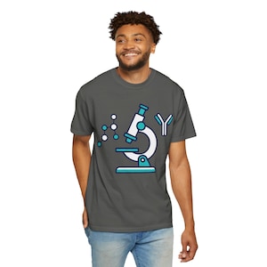 May include: A dark gray short-sleeve t-shirt featuring a graphic print of a white and teal microscope, a molecular structure diagram, and a Y-shaped antibody symbol centered on the chest area of the garment.