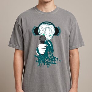 May include: A grey short-sleeve t-shirt featuring a graphic of a white cat with green eyes wearing black headphones and holding a microphone. Below the cat is a dark teal graffiti-style design with the text "HIP HOP..." in a stylized font.