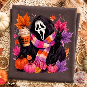 May include: A dark gray fabric featuring a graphic of a hooded figure with a white ghost mask, wearing a pink, orange, and purple striped scarf. The figure holds a coffee cup with a jack-o'-lantern face, surrounded by colorful autumn leaves and pumpkins.