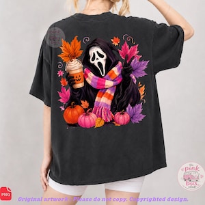 May include: A black short-sleeve t-shirt featuring a graphic of a hooded figure with a white mask, wearing a striped scarf, holding a pumpkin-faced coffee cup, and making a peace sign, surrounded by colorful autumn leaves and orange pumpkins.