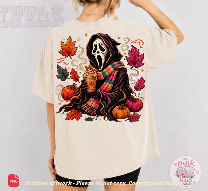 May include: A beige t-shirt featuring a back graphic of a hooded figure with a white mask, wearing a colorful striped scarf and holding a coffee cup. The design includes orange and pink autumn leaves, two pumpkins, and swirling smoke elements.