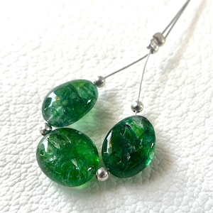 May include: Three oval-shaped, translucent emerald green beads with a cracked internal texture, strung on a thin silver-toned wire. Small, round, metallic silver-coloured spacer beads are positioned between each of the larger green glass beads.