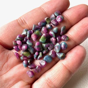 Puede incluir: Una colección de pequeñas piedras pulidas con una mezcla de colores magenta vibrante, rosa intenso y verde bosque. Estas piezas minerales lisas y de forma irregular muestran variaciones de color naturales y una superficie brillante.