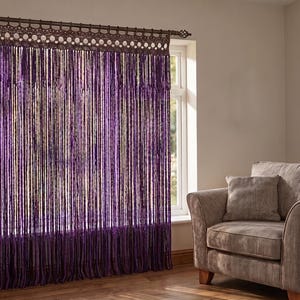 May include: A deep purple string curtain featuring a decorative crocheted top header with circular patterns. The curtain hangs from a dark brown rod mounted above a window, consisting of numerous thin, vertical strands that create a fringe effect.