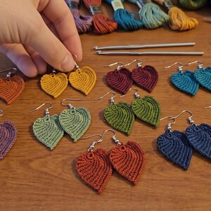 May include: A collection of handmade crochet leaf earrings in various colors including mustard yellow, burgundy, teal, olive green, purple, rust orange, and dusty pink, each featuring a silver-toned metal hook for pierced ears.