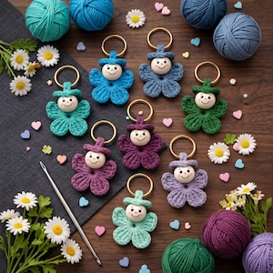 Può includere: Una collezione di otto portachiavi a forma di fiore all'uncinetto con volti in perline di legno, ciascuno dotato di un anello in metallo dorato. Il set include vari colori come blu, verde, viola e turchese, con gomitoli e margherite.