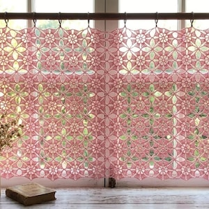 May include: A pink crochet curtain featuring a repeating floral motif pattern. The curtain is suspended from a dark brown wooden rod with metal rings. The intricate openwork design creates a delicate lace-like appearance across the window.