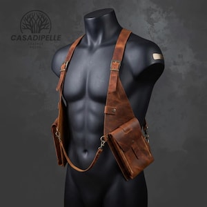 May include: A brown leather shoulder holster bag featuring two vertical pouches with flap closures, adjustable straps with metal buckles, and brass-toned hardware. The logo CASADIPELLE LEATHER HOUSE is visible in the upper left corner of the image.