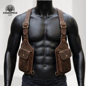 May include: A brown leather chest harness bag featuring two symmetrical pouches with zippered and snap-button closures, adjustable shoulder straps with metal buckles, and D-ring attachments. The logo CASADIPELLE LEATHER HOUSE is visible.