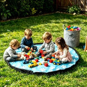 May include: A round, light blue play mat featuring a white paw print pattern, accompanied by a grey felt storage basket with the name Ellie embroidered in white script, and a wooden shelf unit, all filled with colourful plastic building blocks.