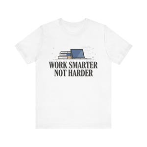 May include: A white short-sleeved t-shirt featuring a graphic of a stack of books next to a laptop. Below the graphic, the text reads WORK SMARTER NOT HARDER in a bold, dark font. The design is centred on the chest of the garment.